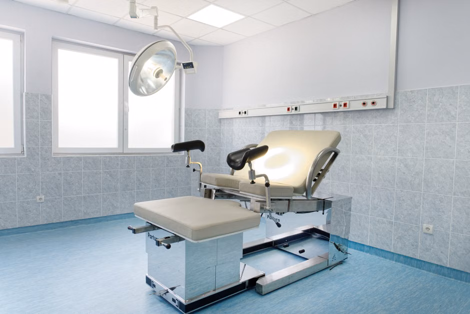 Bright gynecological examination room with adjustable chair and overhead light in a medical facility.